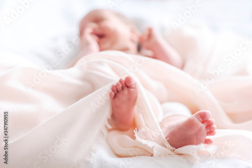Cute newborn baby in white soft blanket after bath. Closeup of infant foot and blur pastel background.
