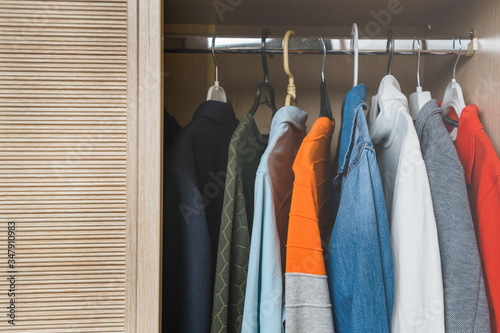 A variety of multi-colored clothes for a teenager hangs in the closet on the hangers.
