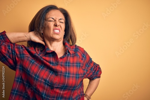 Middle age beautiful woman wearing casual shirt standing over isolated yellow background Suffering of neck ache injury, touching neck with hand, muscular pain