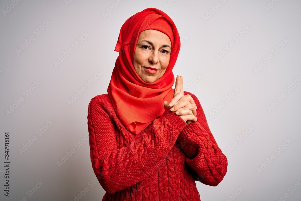Middle age brunette woman wearing muslim traditional hijab over isolated white background Holding symbolic gun with hand gesture, playing killing shooting weapons, angry face Middle age brunette woman wearing muslim traditional hijab over isolated white background Holding symbolic gun with hand gesture, playing killing shooting weapons, angry face