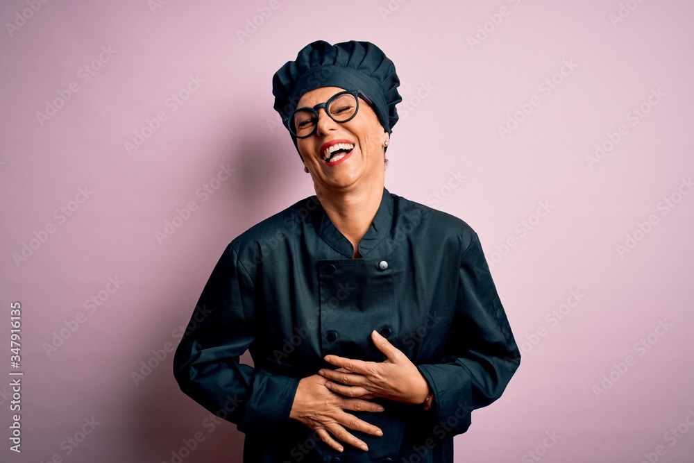 Middle age brunette chef woman wearing cooker uniform and hat over isolated pink background smiling and laughing hard out loud because funny crazy joke with hands on body. Middle age brunette chef woman wearing cooker uniform and hat over isolated pink background smiling and laughing hard out loud because funny crazy joke with hands on body.