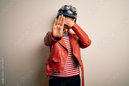 Fotografia Middle age motorcyclist woman wearing motorcycle helmet and jacket over white background covering eyes with hands and doing stop gesture with sad and fear expression