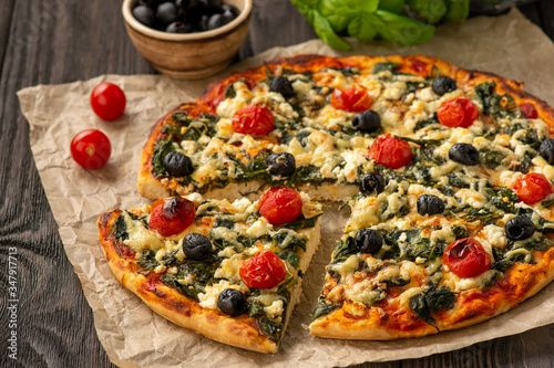 Homemade pizza with spinach, tomatoes and olives.