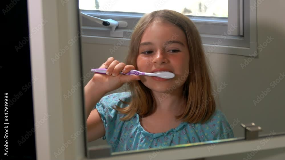 Cheerful beautiful tanned girl in the blue blouse is brushing her teeth in the bathroom next to the window Cheerful beautiful tanned girl in the blue blouse is brushing her teeth in the bathroom next to the window