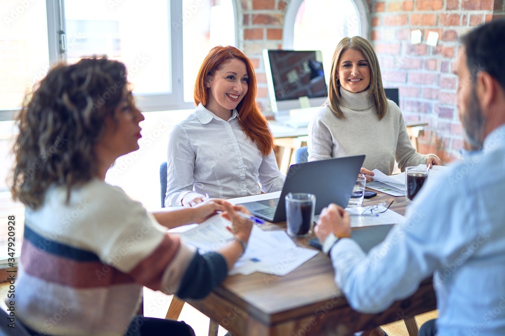 Fototapeta premium Group of business workers smiling happy working together. Sitting with smile on face using laptop reading documents at the office