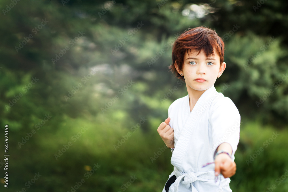 Portrait of short haired 7 years old girl in white kimono making karate kata training outdoors. Martial arts. Sport and activity for children. Japanese combat. Space for text. Portrait of short haired 7 years old girl in white kimono making karate kata training outdoors. Martial arts. Sport and activity for children. Japanese combat. Space for text.