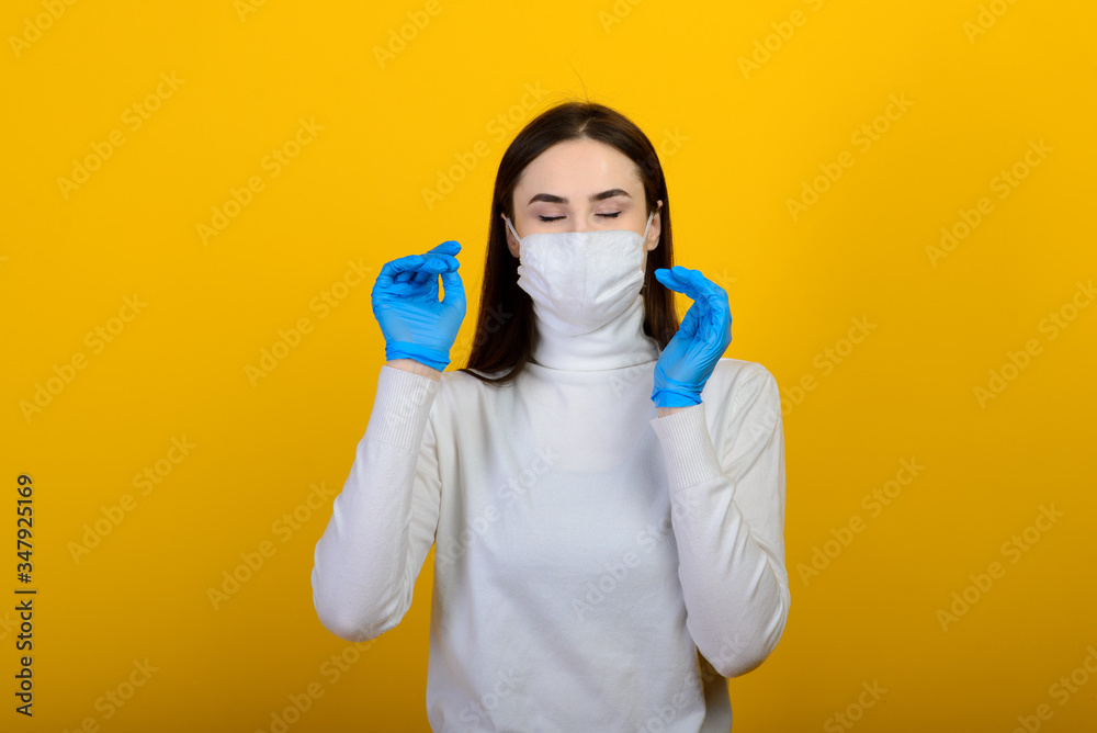 Portrait of a girl in a medical mask, which puts on a rubber glove. Yellow and grey background. Copy space. Portrait of a girl in a medical mask, which puts on a rubber glove. Yellow and grey background. Copy space.
