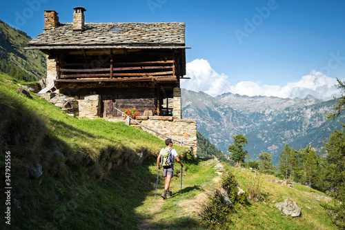 Trekking in the Alps in a beautiful sunny day on a panoramic footpath with ancient traditional Walser house. Aosta Valley, Italy