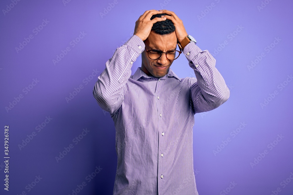 Handsome african american man wearing striped shirt and glasses over purple background suffering from headache desperate and stressed because pain and migraine. Hands on head.