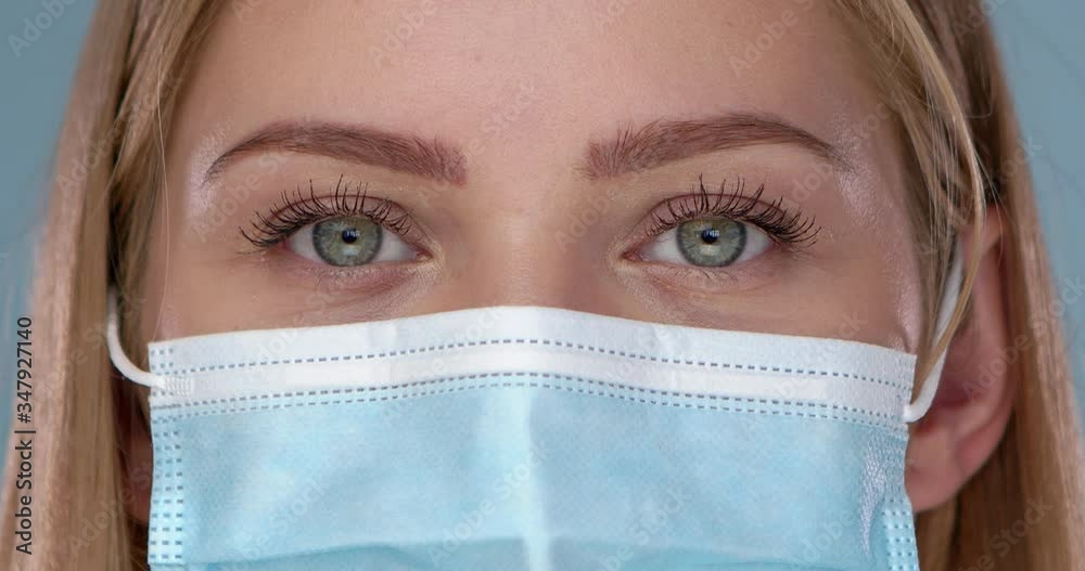 Young woman posing in medical face mask. Looking at camera with smile behind