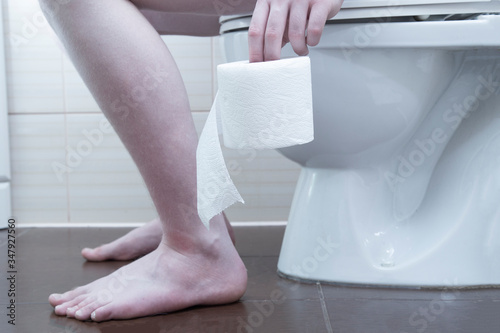 Toilet paper. A person is sitting on the toilet and holding toilet paper. photo