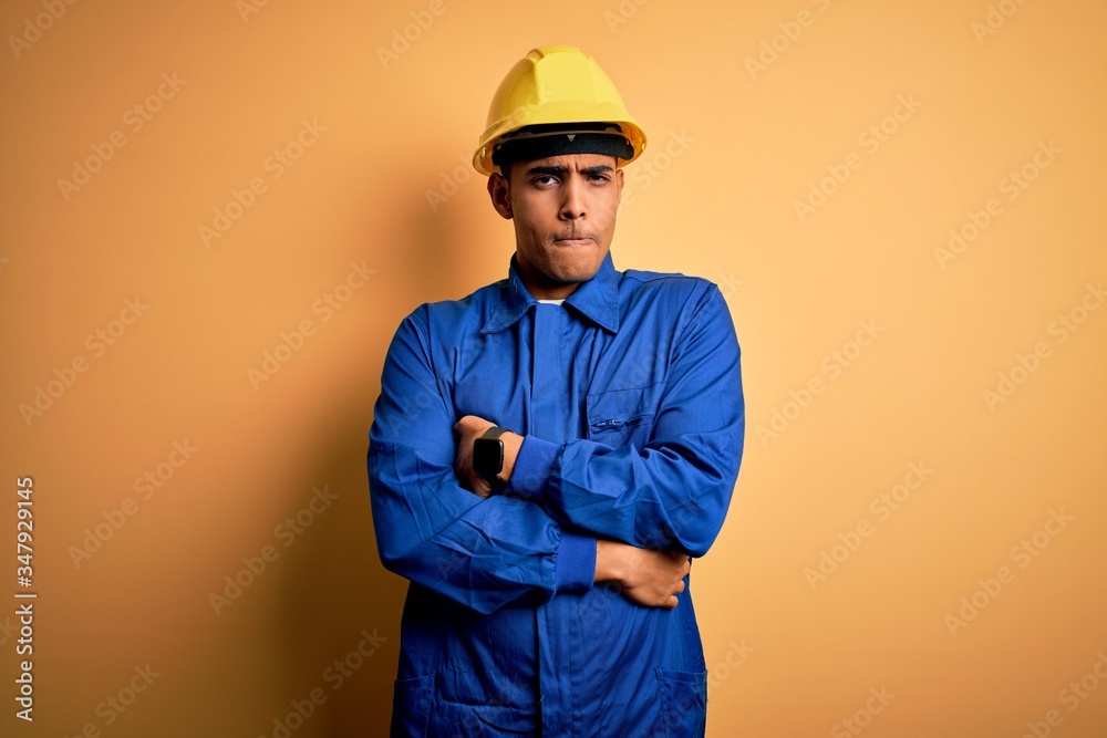 Young handsome african american worker man wearing blue uniform and security helmet shaking and freezing for winter cold with sad and shock expression on face