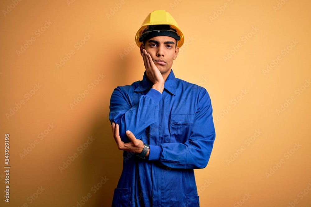 Young handsome african american worker man wearing blue uniform and security helmet thinking looking tired and bored with depression problems with crossed arms.