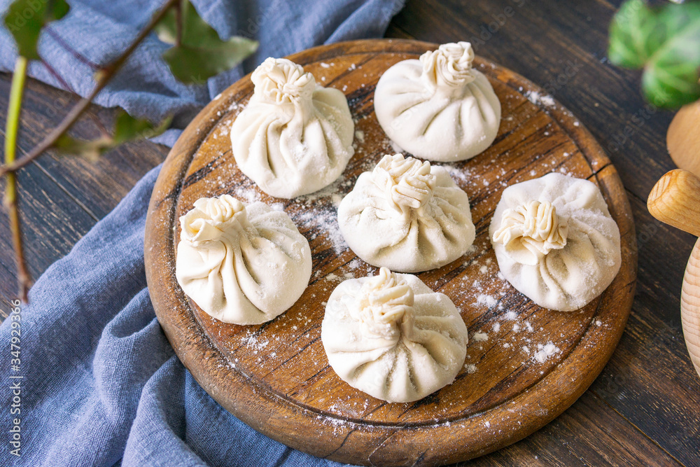 Homemade raw Khinkali - Georgian name of traditional dumplings with meat on wooden round plate close up, before cooking. Rustic table, natural beautiful light. Selective focus, copy space.