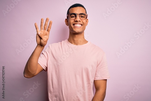Handsome african american man wearing casual t-shirt and glasses over pink background showing and pointing up with fingers number four while smiling confident and happy. © Krakenimages.com