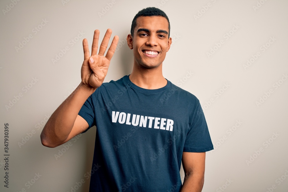 Young handsome african american man volunteering wearing t-shirt with volunteer message showing and pointing up with fingers number four while smiling confident and happy.