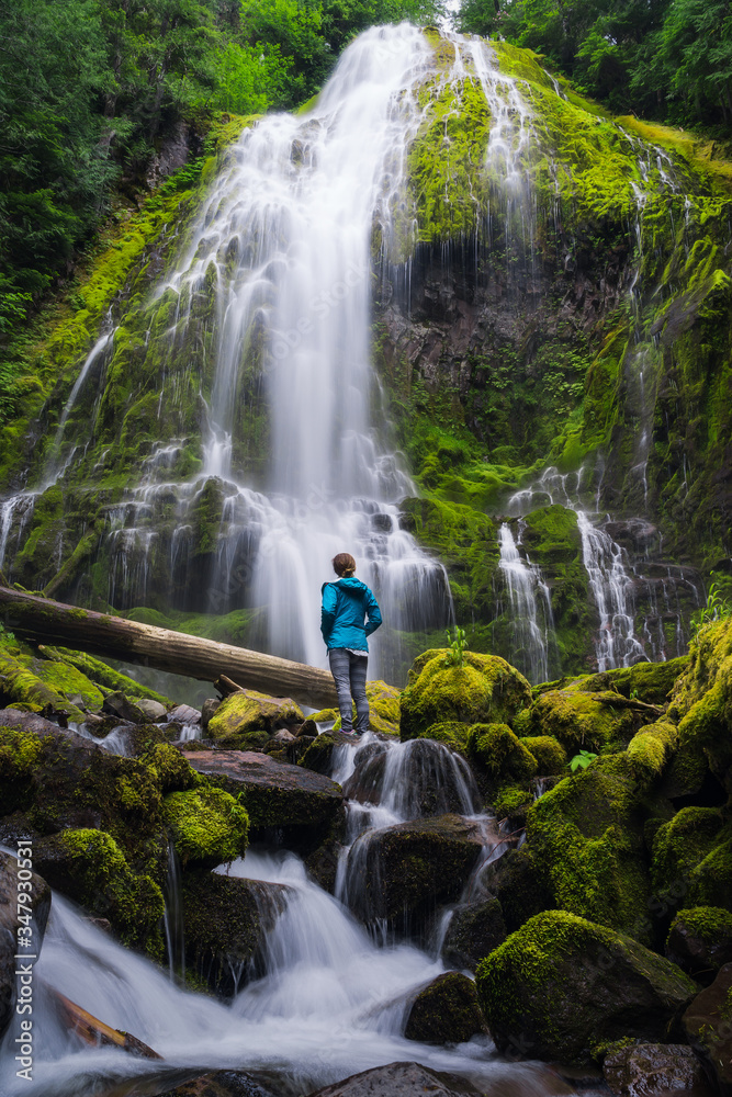 Young woman looking up at huge waterfall in forest Young woman looking up at huge waterfall in forest