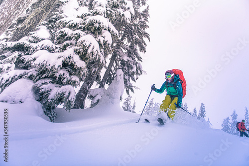 Woman jumping from top of snowy hill while backcountry skiing in BC
