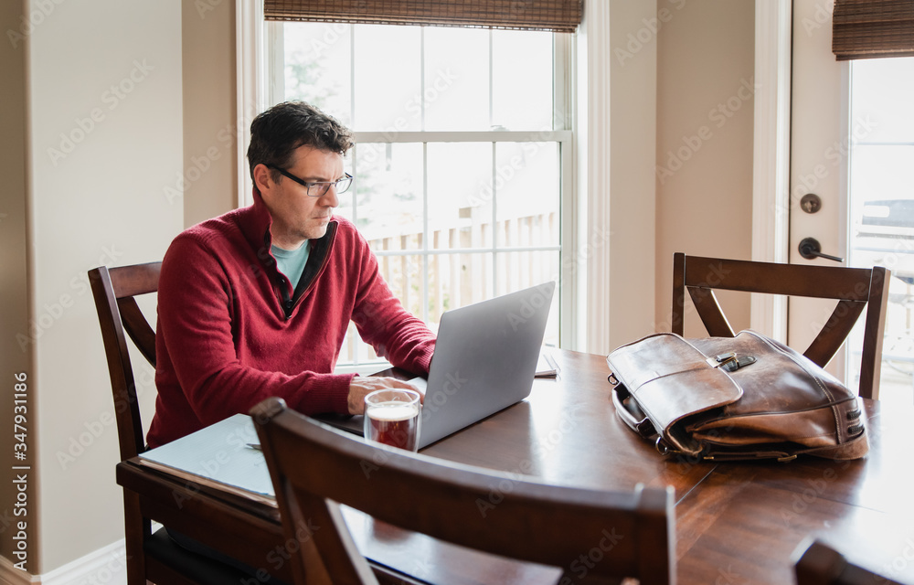 Man in glasses working from home using a computer at a dining table. Man in glasses working from home using a computer at a dining table.