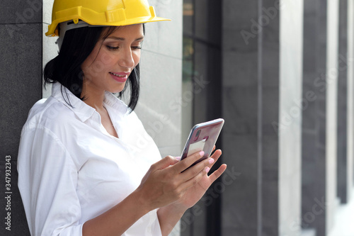 Half figure portrait of smart succdessful engineer woman smiling, using smartphonecomputer infront of office building in downtown urban area and ready to work.