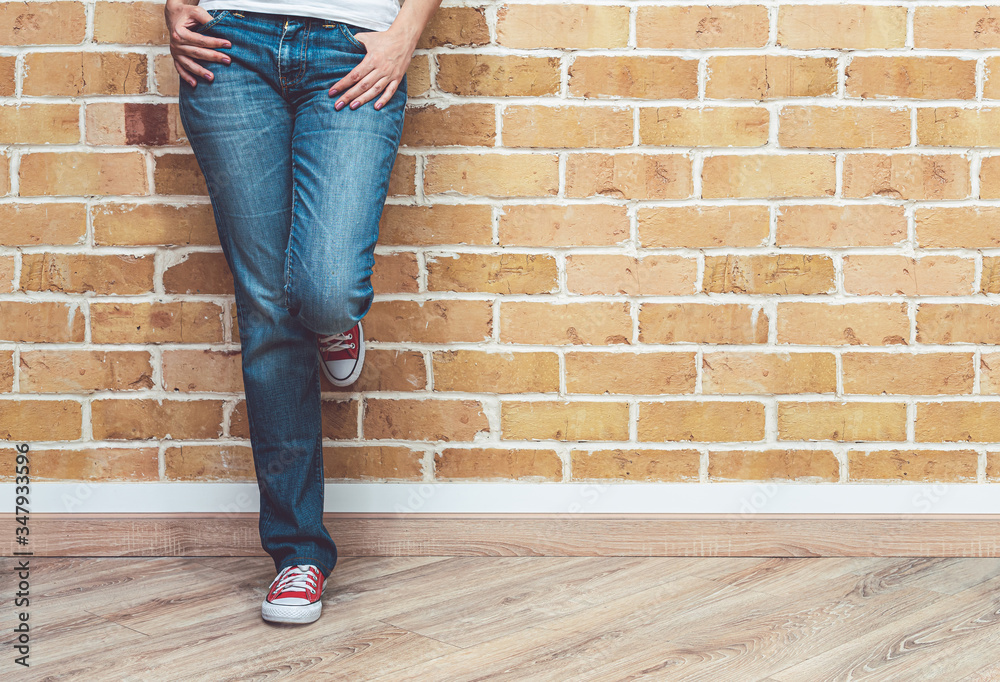 Woman legs in jeans and red sneakers, woman standing in front of brick wall, fashion concept Woman legs in jeans and red sneakers, woman standing in front of brick wall, fashion concept
