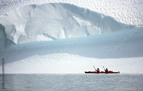 two men rowing their sea kayak along an iceberg in Greenland photo