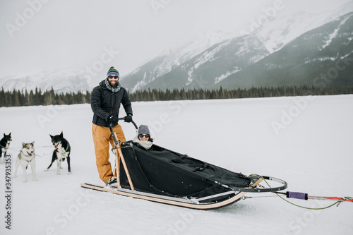 man and woman couple sit and stand in dogsled in canadian rockies