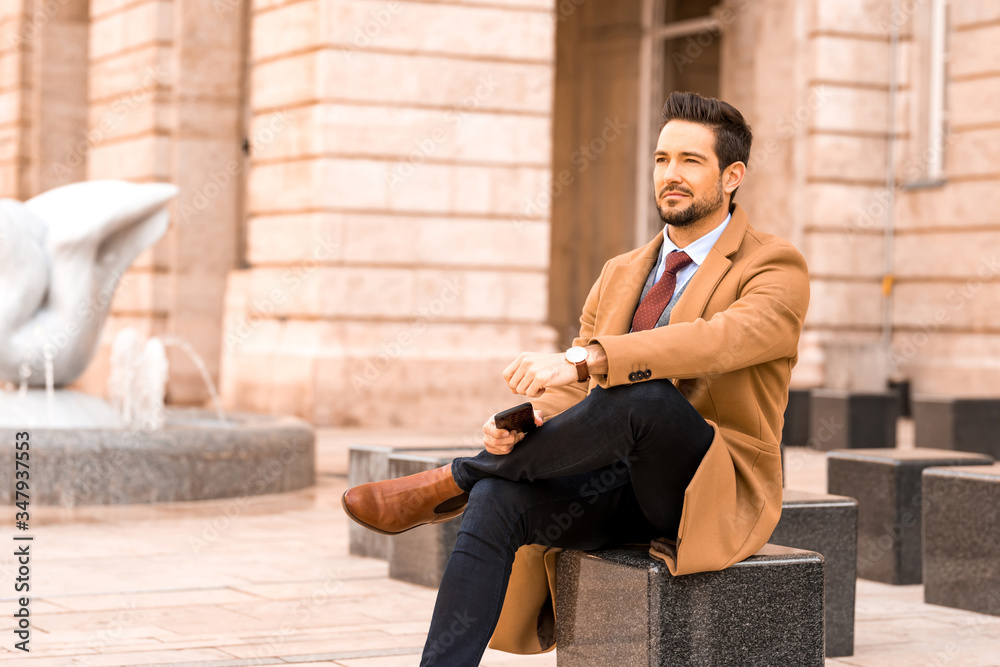 An elegant man sitting next to a fountain An elegant man sitting next to a fountain