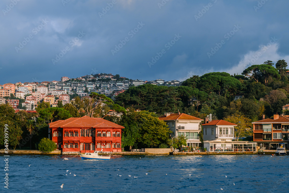Beautiful and luxurious mansions and houses over the hills at the shore of Bosphorus strait and a boat passing by in front of the houses on a sunny day.