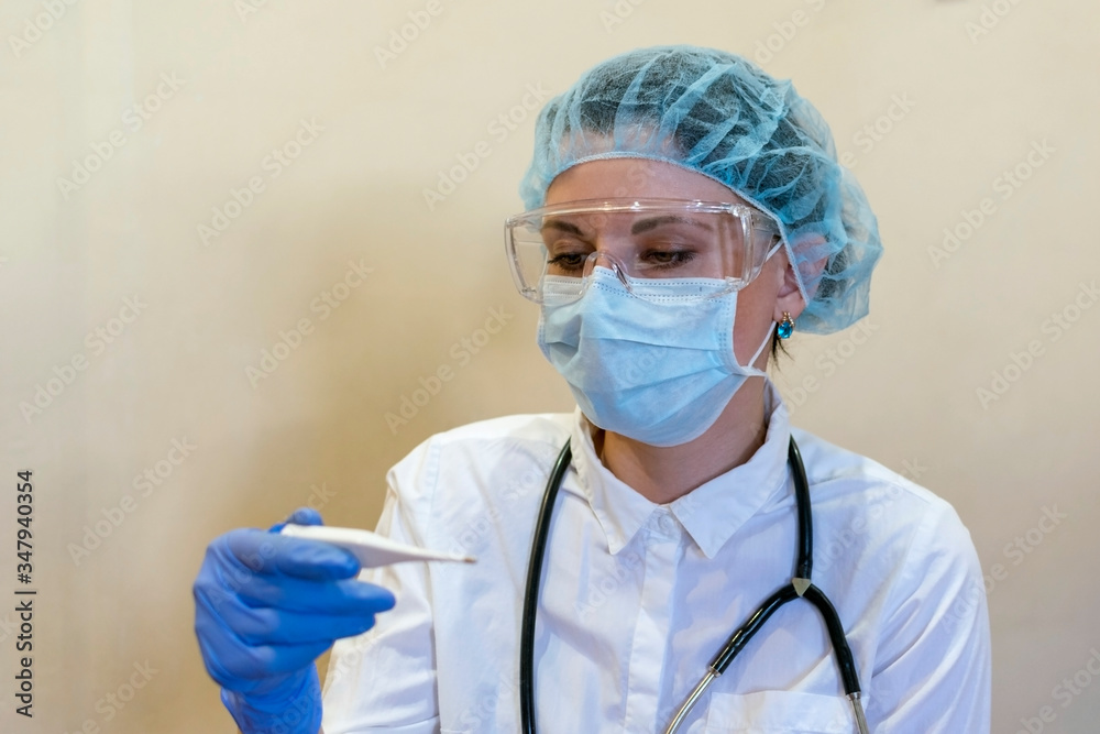 A doctor in a medical mask looks at the thermometer. A doctor in a medical mask looks at the thermometer.