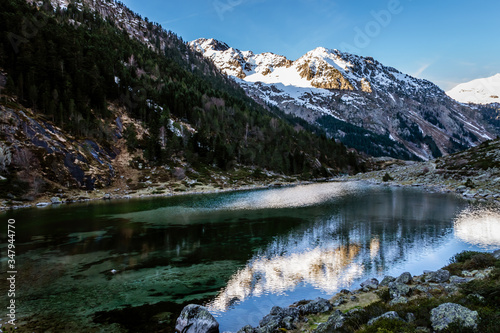 A picturesque landscape view of the high snow capped Pyrenees mountains on a winter evening and a lake with still water  Lac de Suyen  Arrens-Marsous  Hautes-Pyrenees  France 