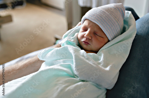 Newborn baby asleep, swaddled in hospital blanket and wearing a hat