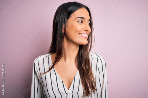 Fotografie Young beautiful brunette woman wearing casual striped shirt over isolated pink background looking away to side with smile on face, natural expression
