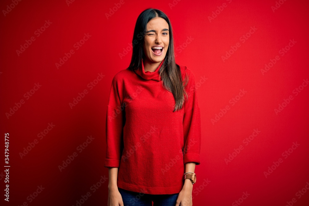 Fototapeta premium Young beautiful brunette woman wearing casual sweater over isolated red background winking looking at the camera with sexy expression, cheerful and happy face.