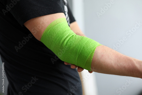 Man shows stretching on arm with elastic bandage