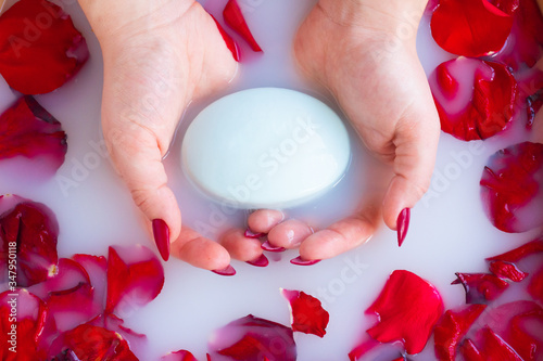 Top view female hands hold soap against the background of milk or white water with rose petals