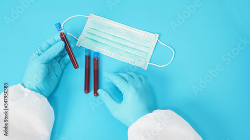 Male model with PPE suite and Hand wearing glove is holding face mask. Blood collection tubes on blue background.