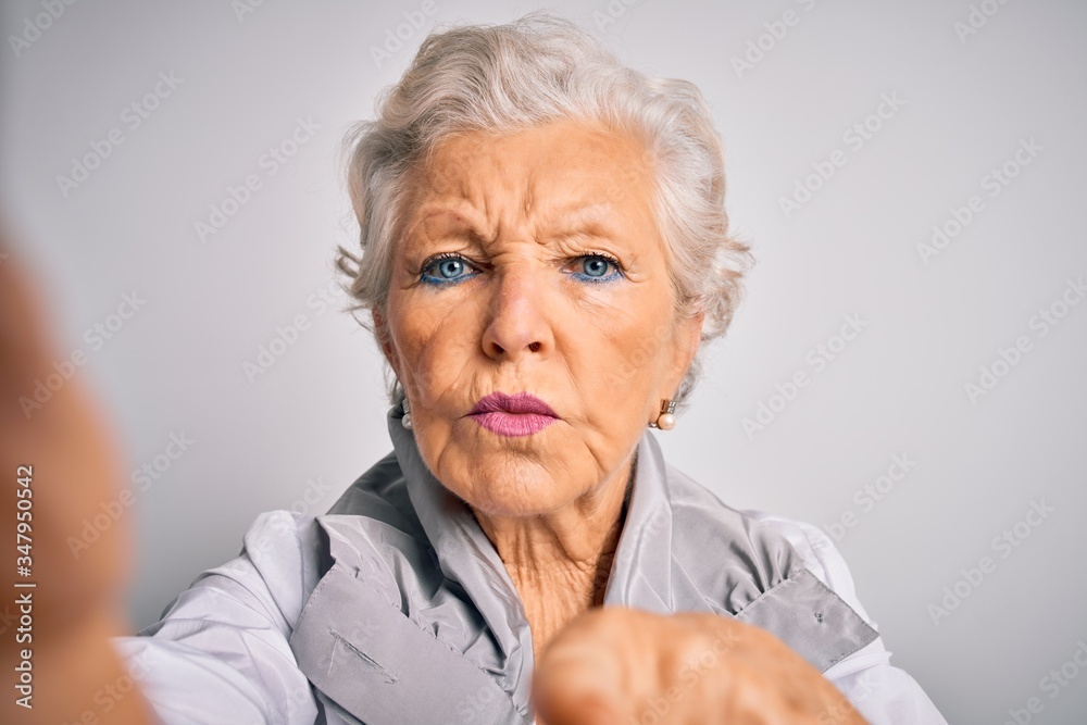 Senior beautiful grey-haired woman making selfie by camera over isolated white background pointing with finger to the camera and to you, hand sign, positive and confident gesture from the front