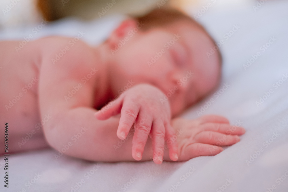 Calm cute infant with closed eyes covered with blanket resting in bed against blurred interior of light bedroom Calm cute infant with closed eyes covered with blanket resting in bed against blurred interior of light bedroom