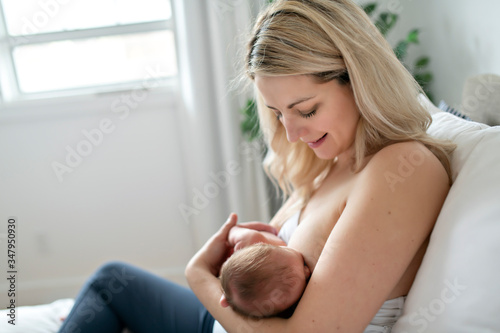 Fotografie woman in her bedroom on the white cushions, smiling and breastfeed her baby