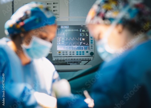 Modern monitor showing vital signs of patient while surgeon and assistant performing operation in modern hospital photo