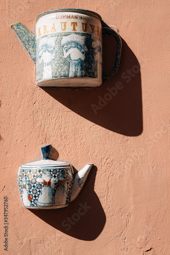 Old brown ceramic teapot on wall. Element decor in Vilnius street. Street art in Lithuania. Sunny day. Tableware   as decoartion of exterior. Outdoor decor as walled kettle. Urbun Lietuva craft art. photo