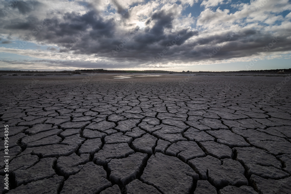 From above of drought cracked lifeless ground under colorful cloudy sky From above of drought cracked lifeless ground under colorful cloudy sky