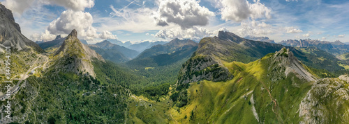 Italian Dolomites mountain valley. Aerial beautiful shot above the clouds. Green hills with forests and rocks. Mountain fields. Amazing nature, Italy location. Postcard and ecological concept.