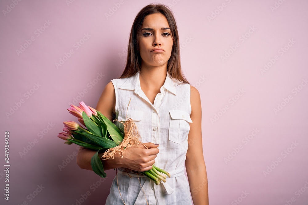Young beautiful brunette woman holding bouquet of tulips flowers over pink background depressed and worry for distress, crying angry and afraid. Sad expression. Young beautiful brunette woman holding bouquet of tulips flowers over pink background depressed and worry for distress, crying angry and afraid. Sad expression.