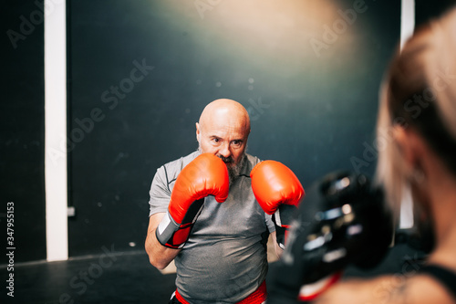 Back view of cropped unrecognizable young sportswoman athlete in boxing gloves training fighting with professional male coach in modern gym photo