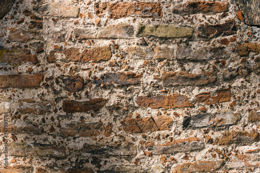 Fototapeta premium Old brick wall texture. Weathered wall surface. Grungy orange brickwall. Red stonewall background. Shabby building facade on sunny day. Old brown stone wall in city. Vintage backdrop with row brick.