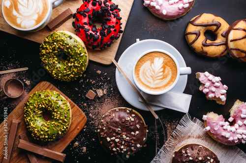 Various doughnuts with sweet toppings and chocolate bars composed with cup of cappuccino on black table photo