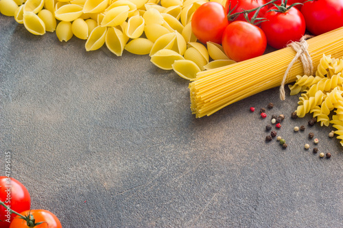 Frame with spaghetti and various ingredients for cooking pasta on a dark background, top view