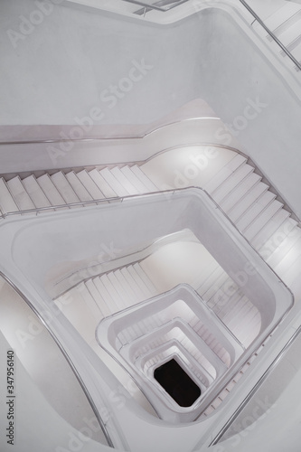 From above of light concrete spiral stairway with ornamental metal banister in modern white building